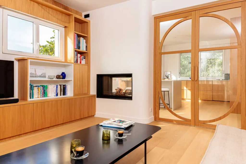 Installation d'une cheminée sur-mesure Rüegg Violino par Cheminées Nicolas dans un salon moderne avec menuiserie en bois clair.