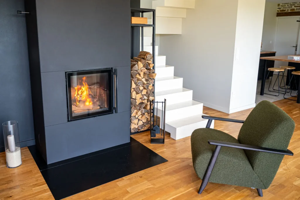 Gros plan sur la vitre du poêle à accumulation Tulikivi Raita 21 en fonctionnement avec un porte-bûches design en métal noir.